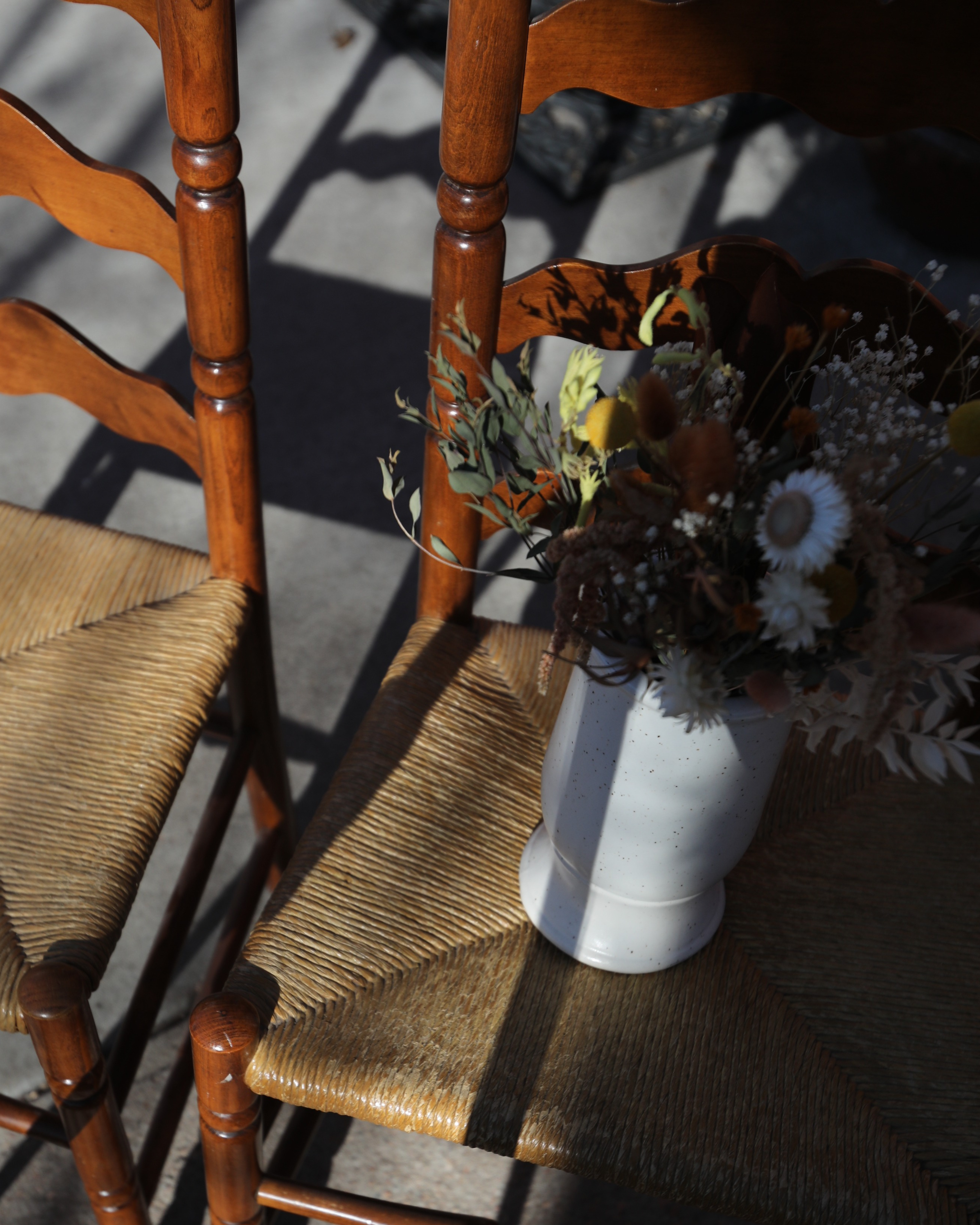 Two ladder back chairs with a vase of flowers.
