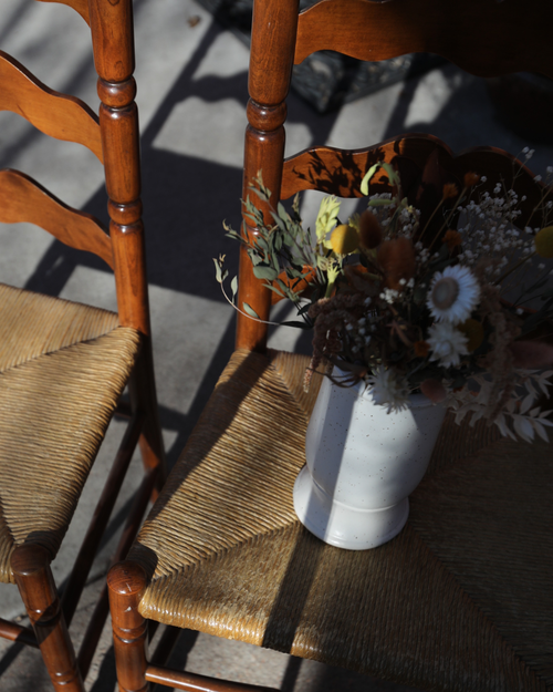Two ladder back chairs with a vase of flowers.